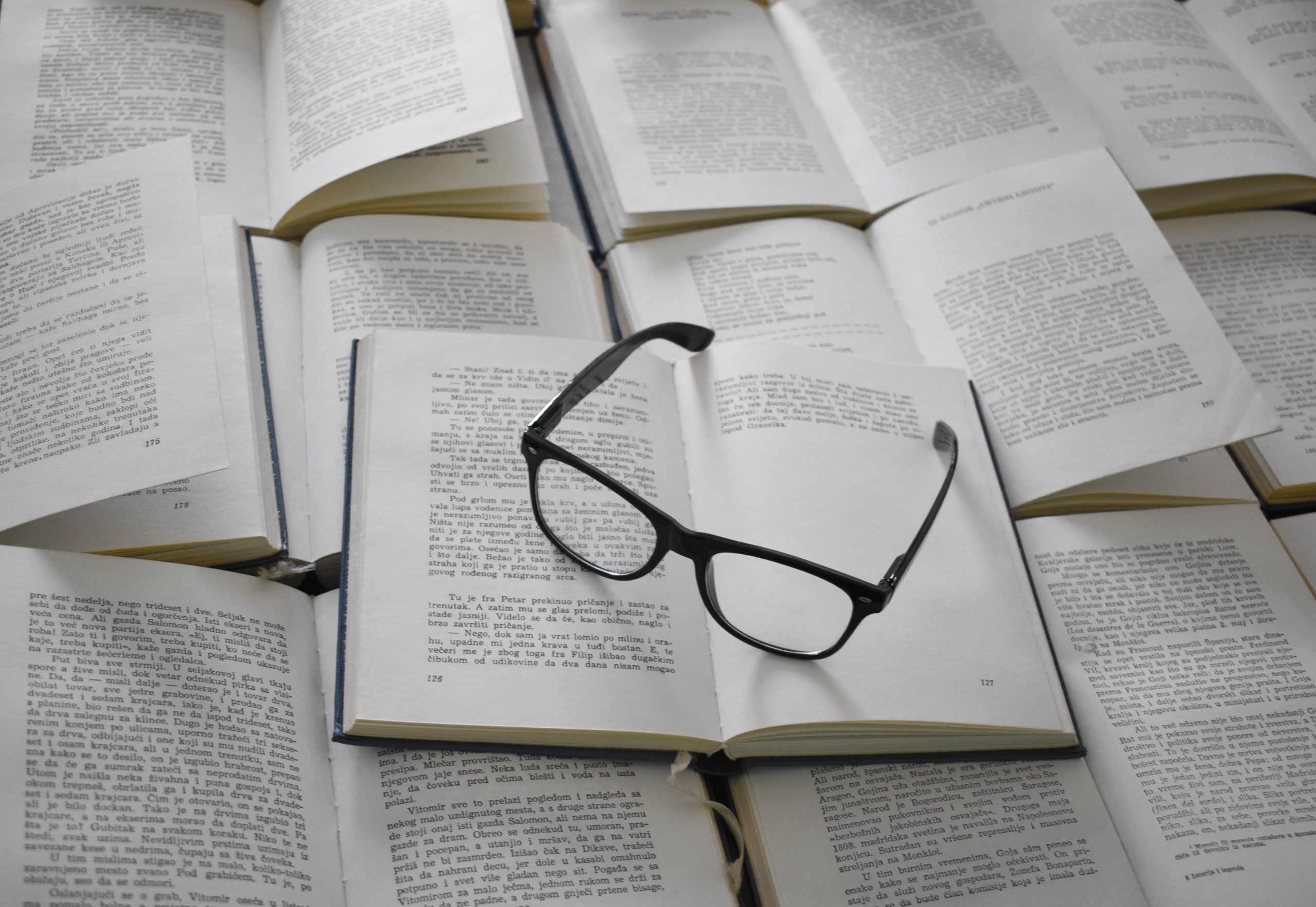 Many open books with eyeglasses on sitting on top
