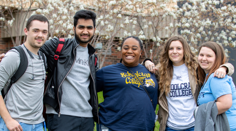 group of five students smiling outdoors campus