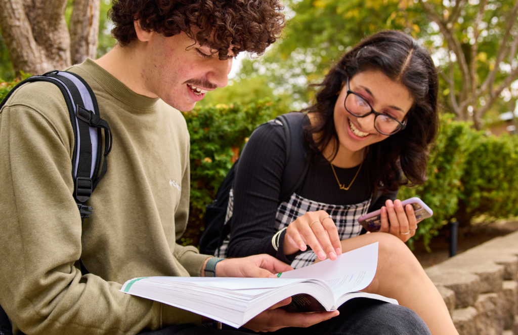 two students reading a book together outdoors