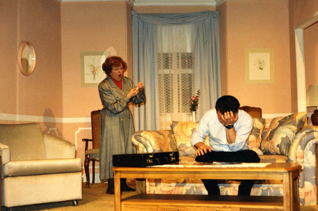 A staged scene discussion between people in a living room setting.