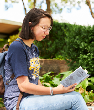 Student sits outside reading a book