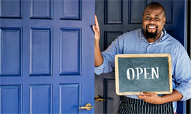 Man holding an "open" sign outside of a business
