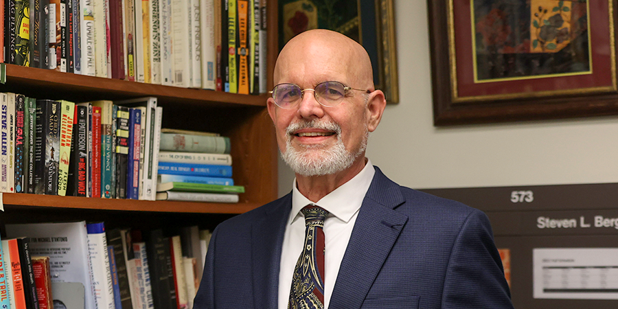 Headshot of writer sitting in front of bookshelf smiling