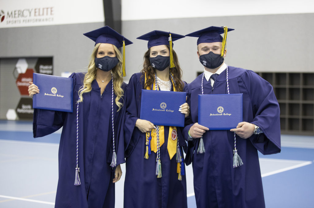 Students in regalia holding up degrees