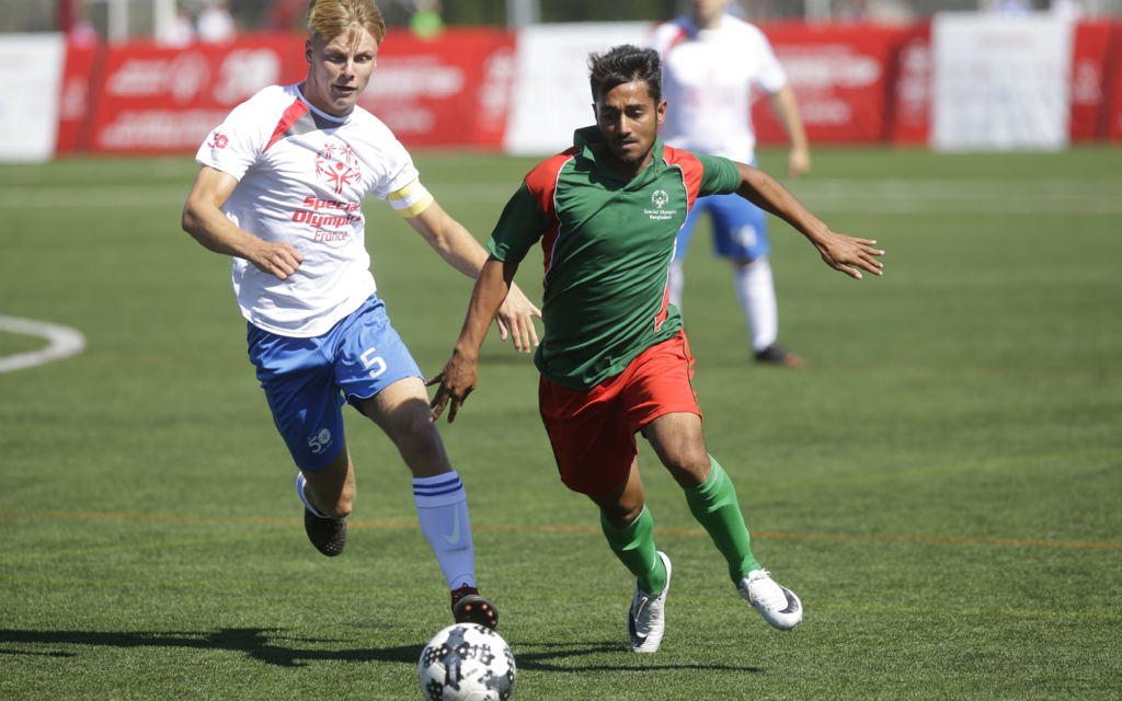 two opponents run toward soccer ball