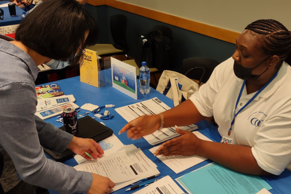 A person working at a table presents pamphlets to an attendee