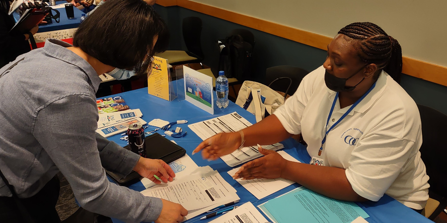 A person working at a table presents pamphlets to an attendee