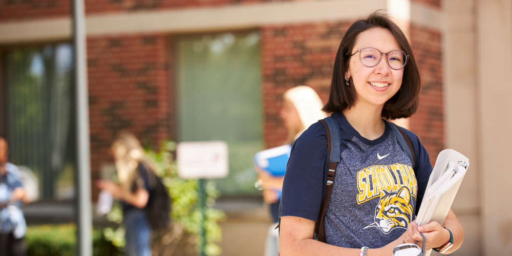 student holding binder smiling