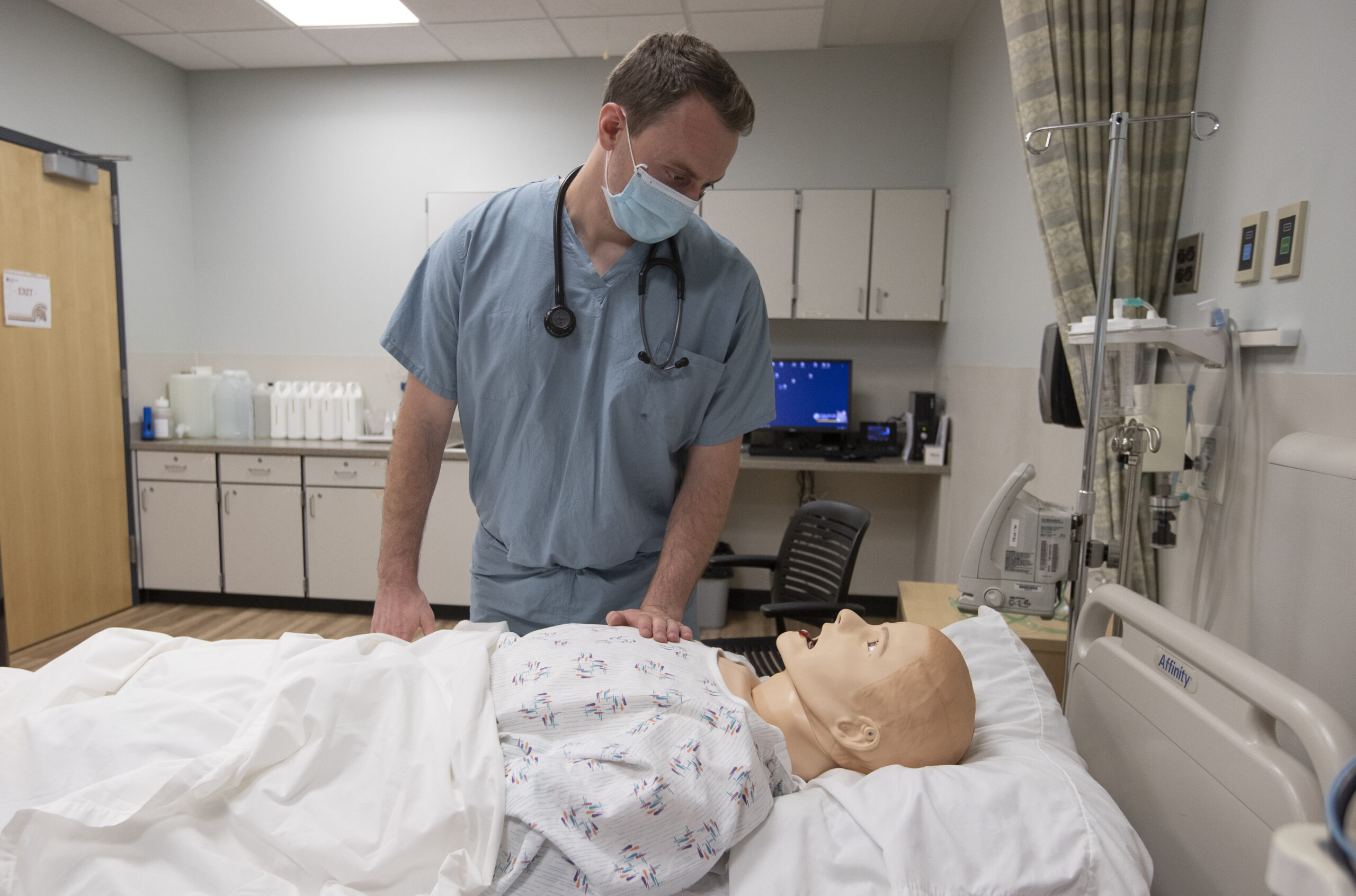 nursing student looking down at bed patient manikin