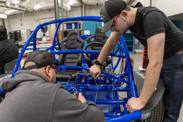 student working on frame metal of a car