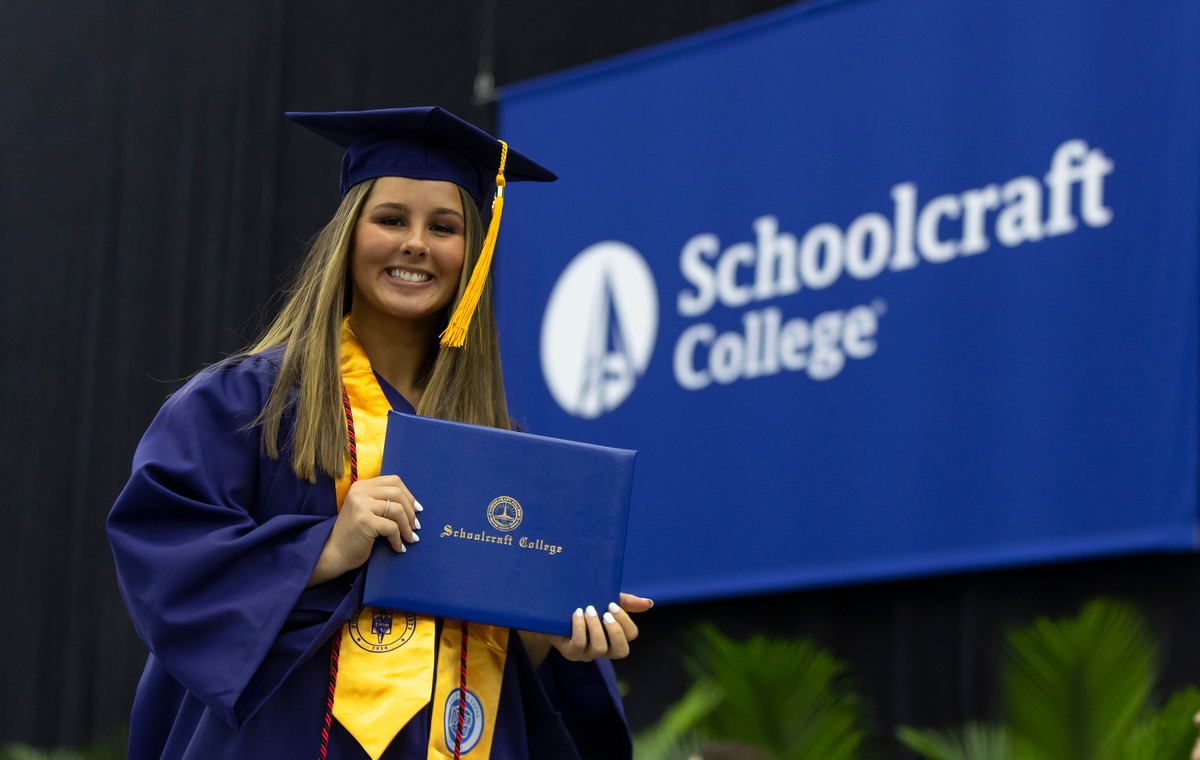 grad in regalia holding up diploma smiling