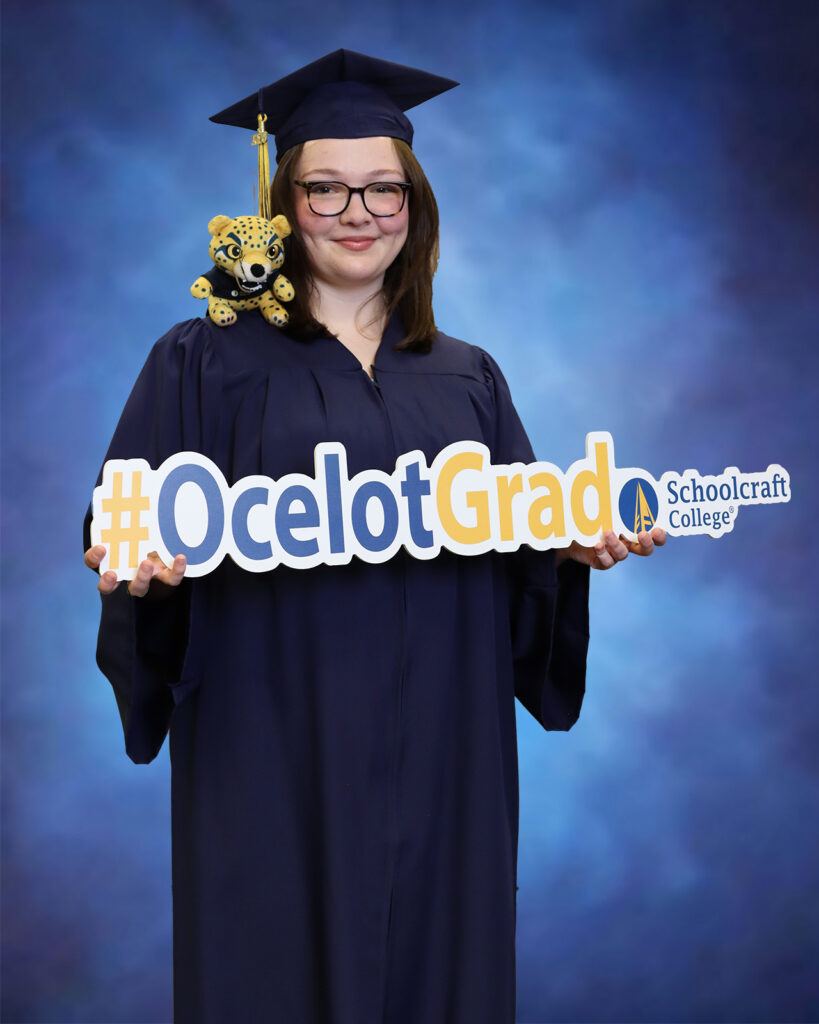 Addison with ocelot plush on shoulder, holding Ocelot Grad sign