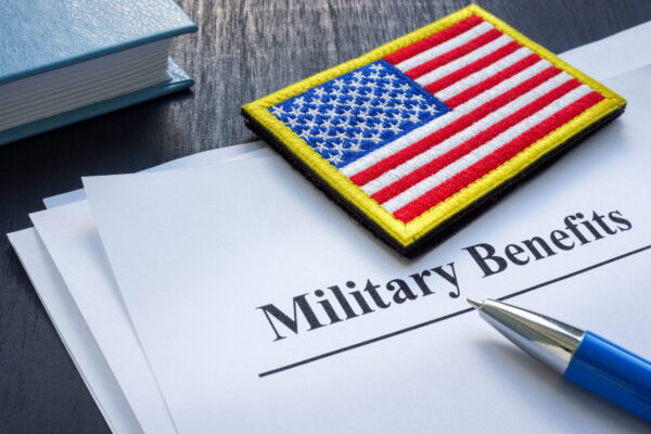 a piece of paper titles "military benefits" with an american flag patch and a pen on top.