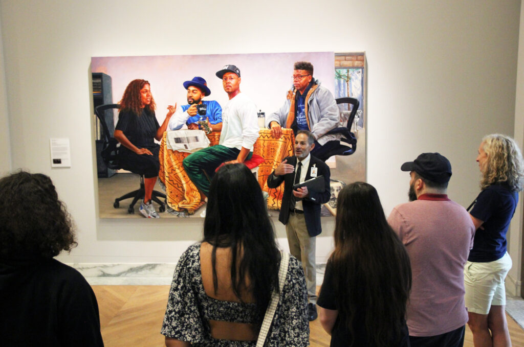 people looking at a painting on the wall while a guide discusses the piece.