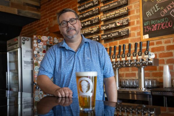 man wearing a blue shirt standing in front of a beer on a table