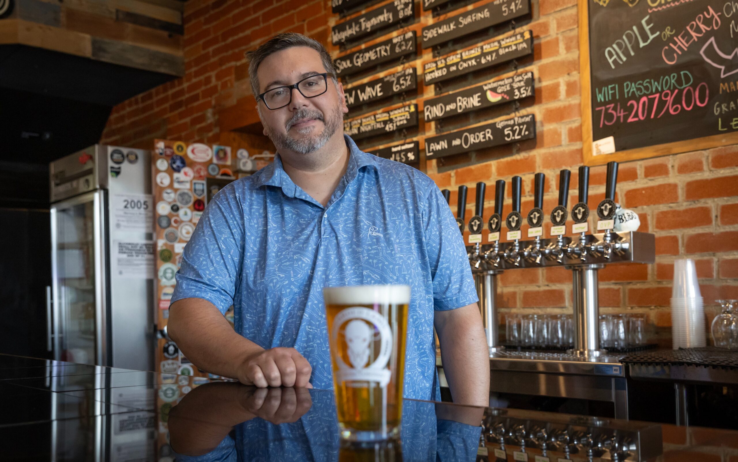 man wearing a blue shirt standing in front of a beer on a table